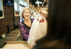 A mature woman taking a shopping bag from the cashier at a supermarket where there is no plastic bag ban.